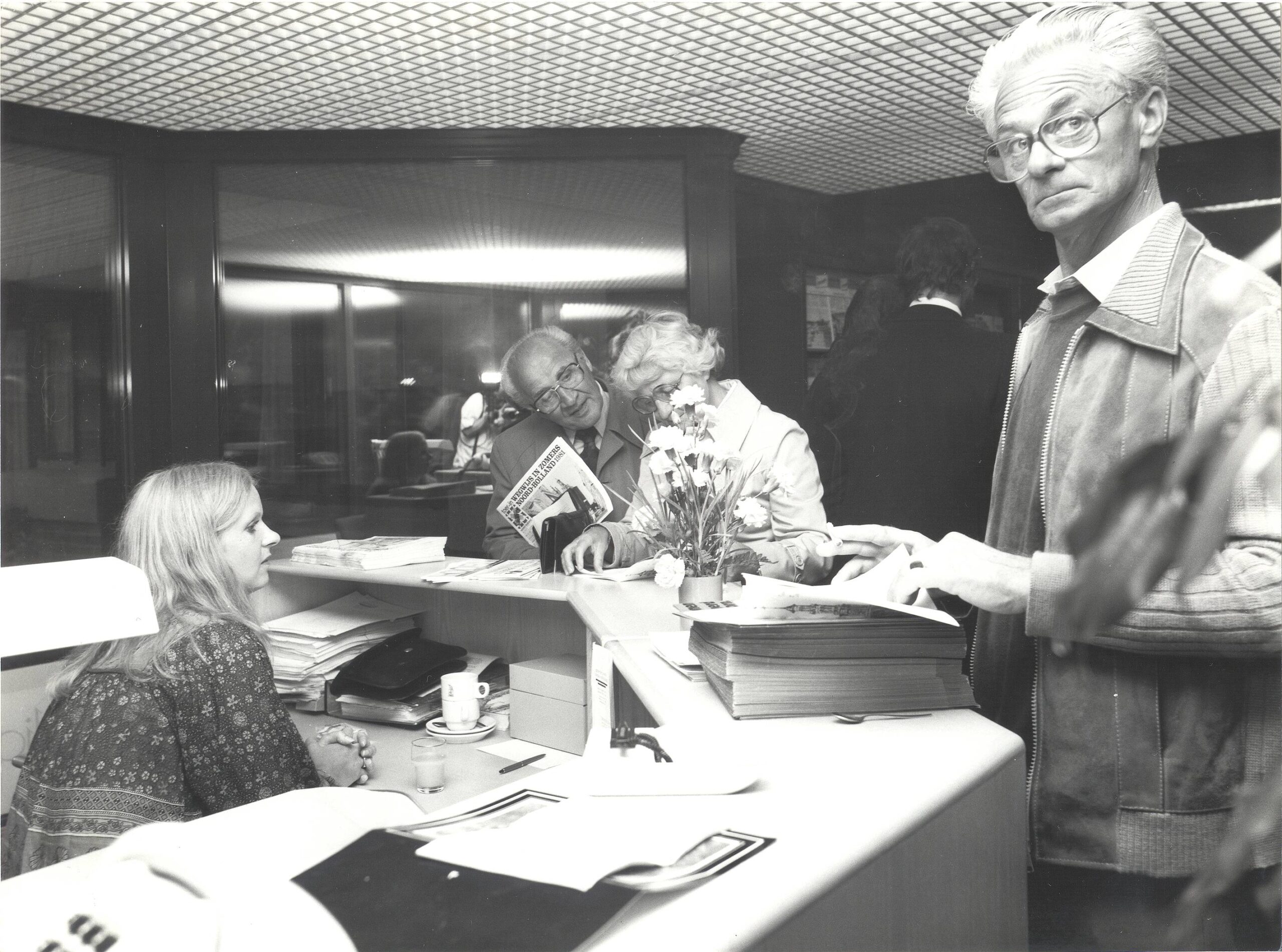 Mensen staan bij een balie en bladeren door papieren.